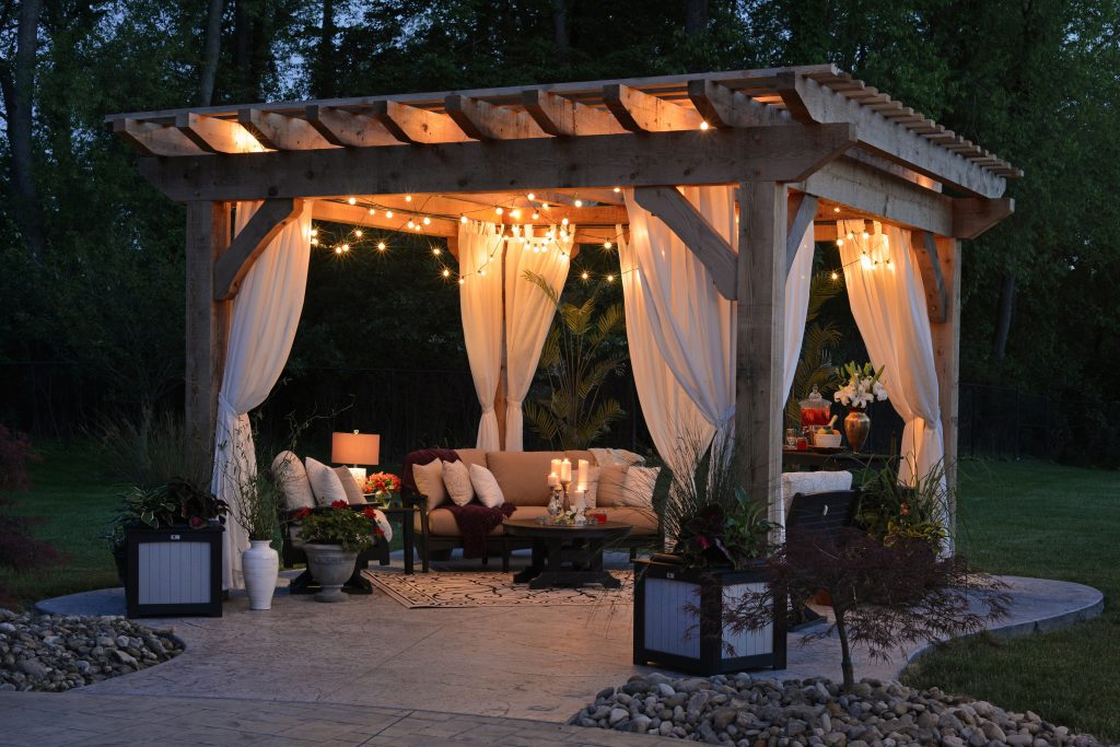 A patio is lit up with an array of hanging lights, draped curtains and lanterns