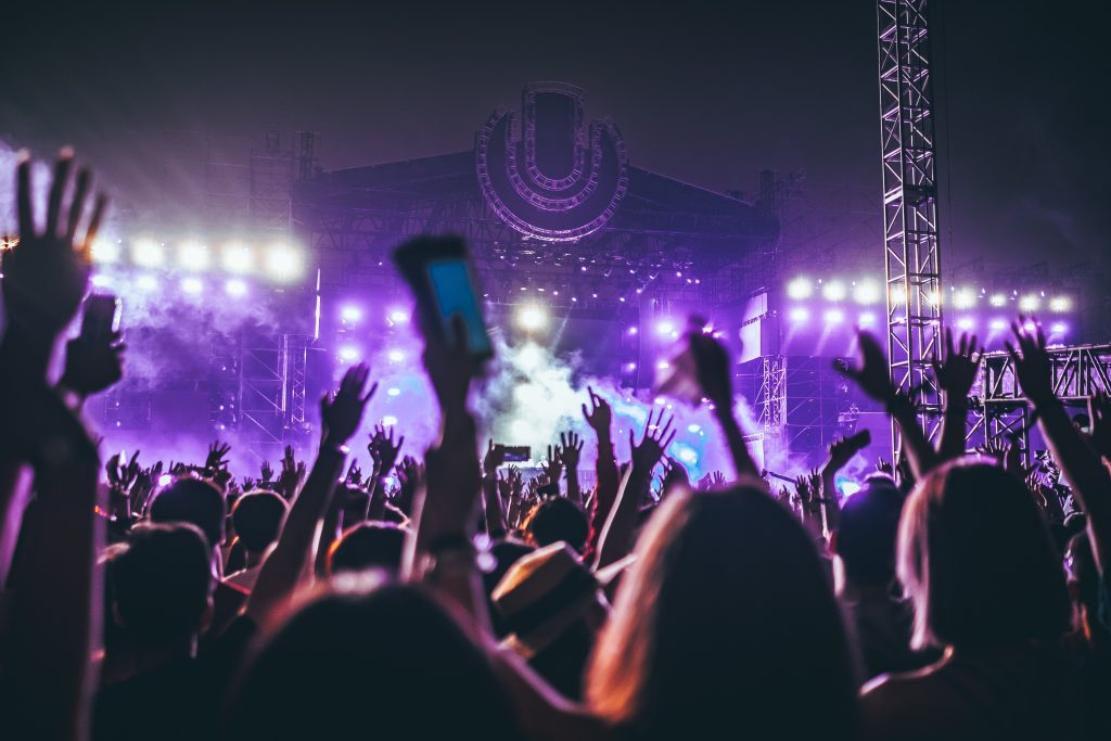 Music lovers converge on a 3-day music festival, bright purple lights illuminate the night sky.