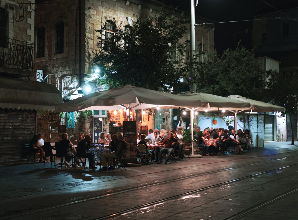 A patio illuminated with proper lighting and patio umbrellas is shown full of lively patrons.