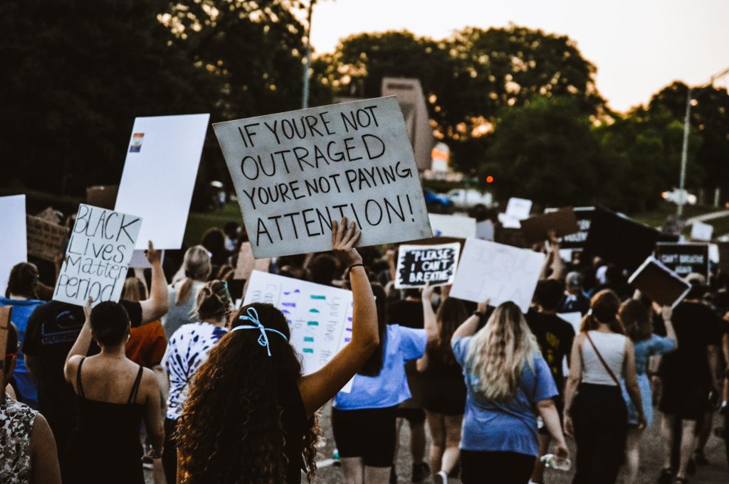 A protester holds a sign that reads "If you're not outraged, you're not paying attention"