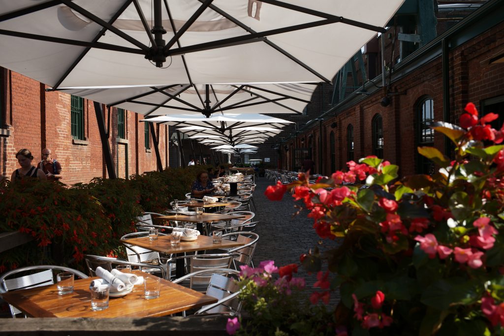 A restaurants outdoor patio is shown, with proper shading and plants to give off a nice atmosphere.
