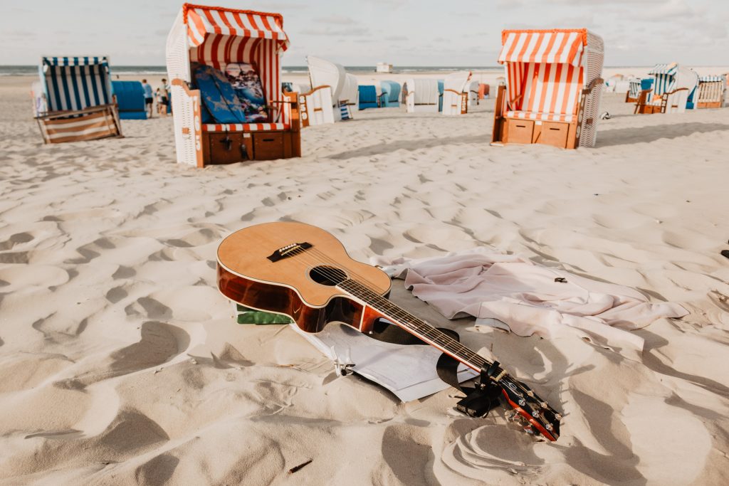 A guitar lays in the sand, depicting the importance of having appropriate music for the summer in a retail store