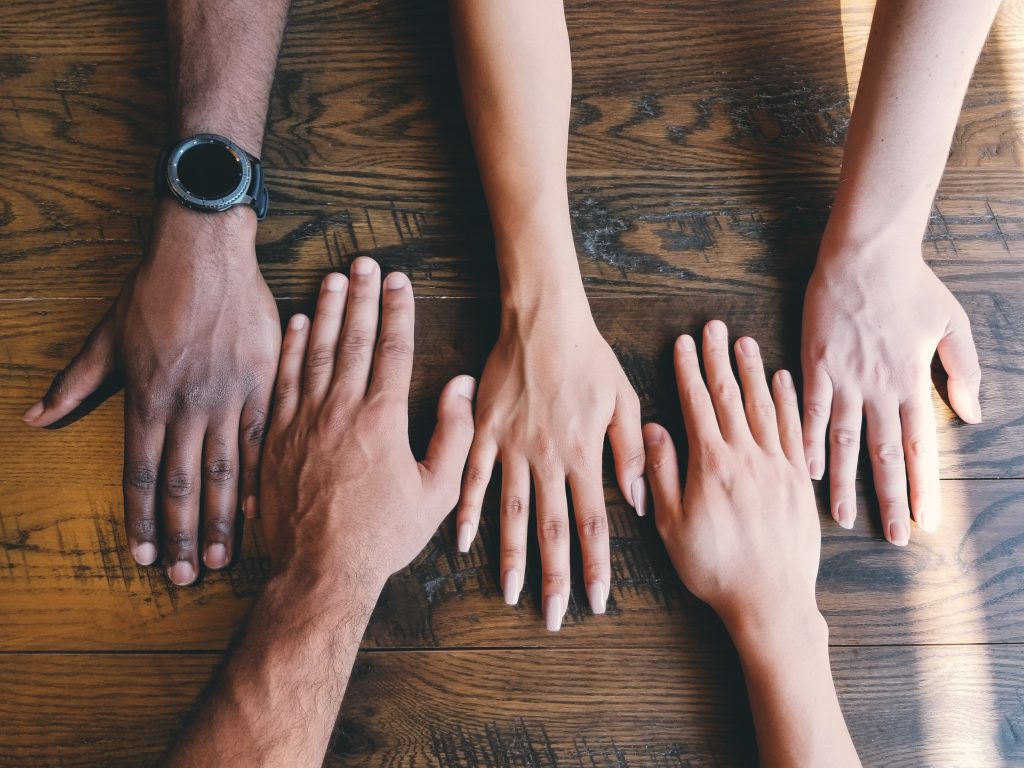 Un groupe d'amis diversifiés pose les mains sur une table pour montrer leur différence de couleur de peau.