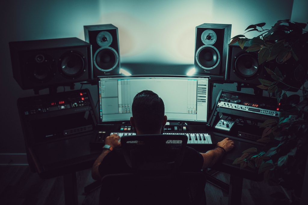 A producer is seated at his production set up in a dimly lit studio.