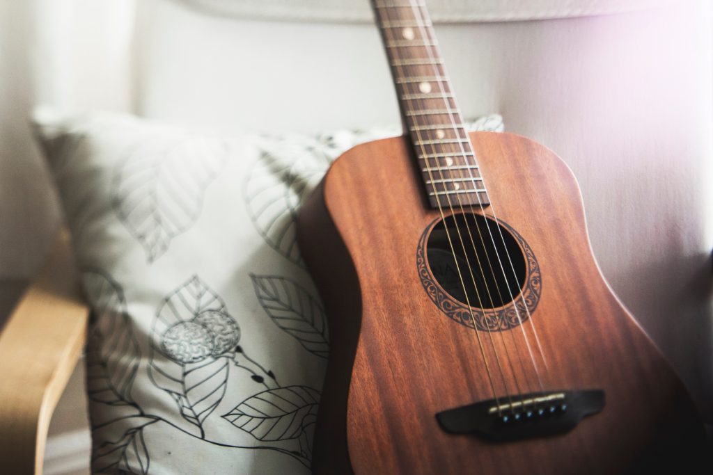 A guitar rests on a pillow while on a couch.