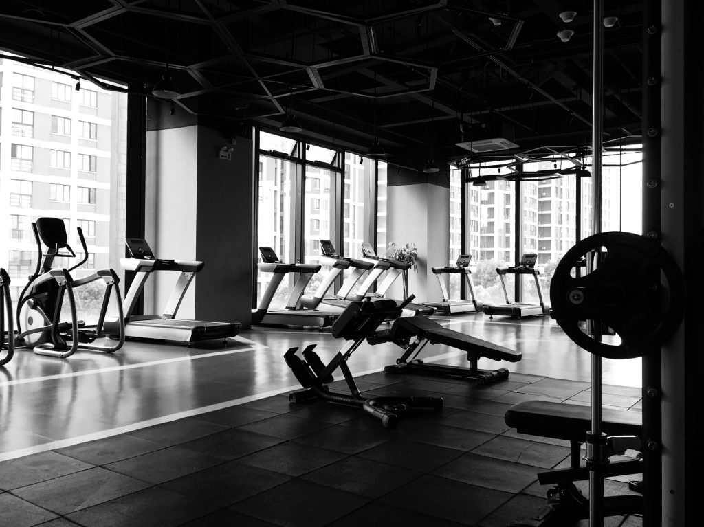 A black and white photo of a gym showcases treadmills, weights and other equipment.