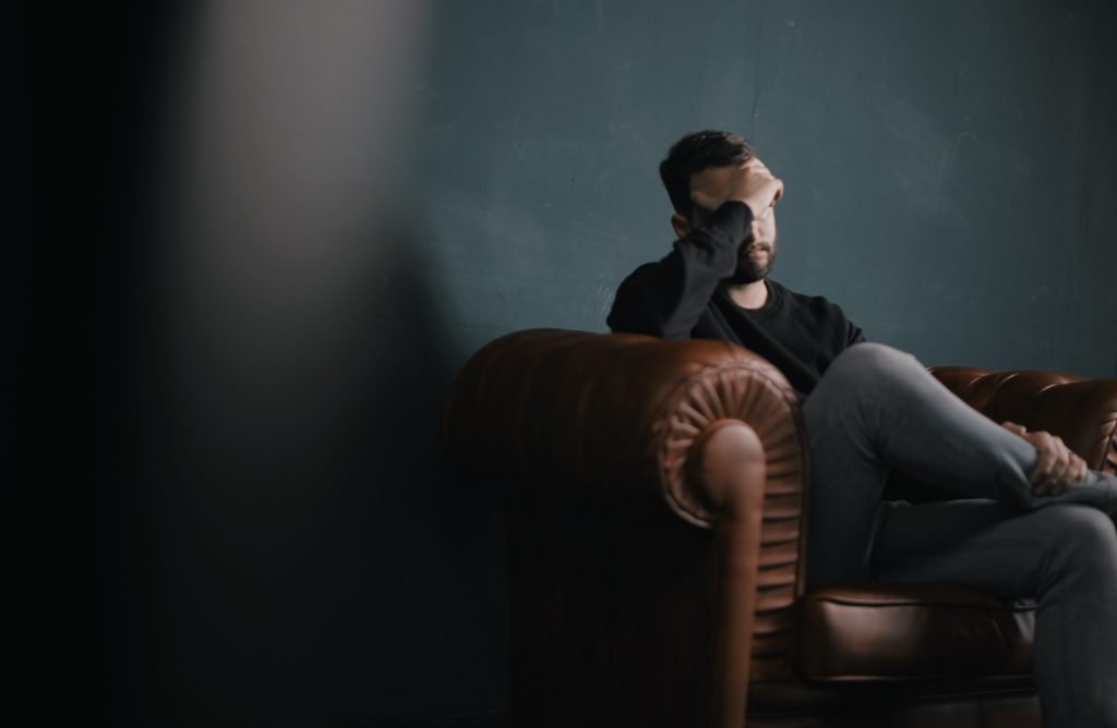 A man sits in a chair with his hand on his head, during a music therapy session.