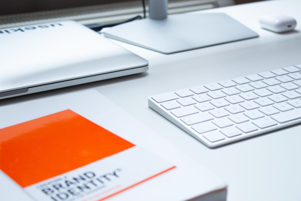 A white desk is shown with a keyboard and book with the title "brand identity"