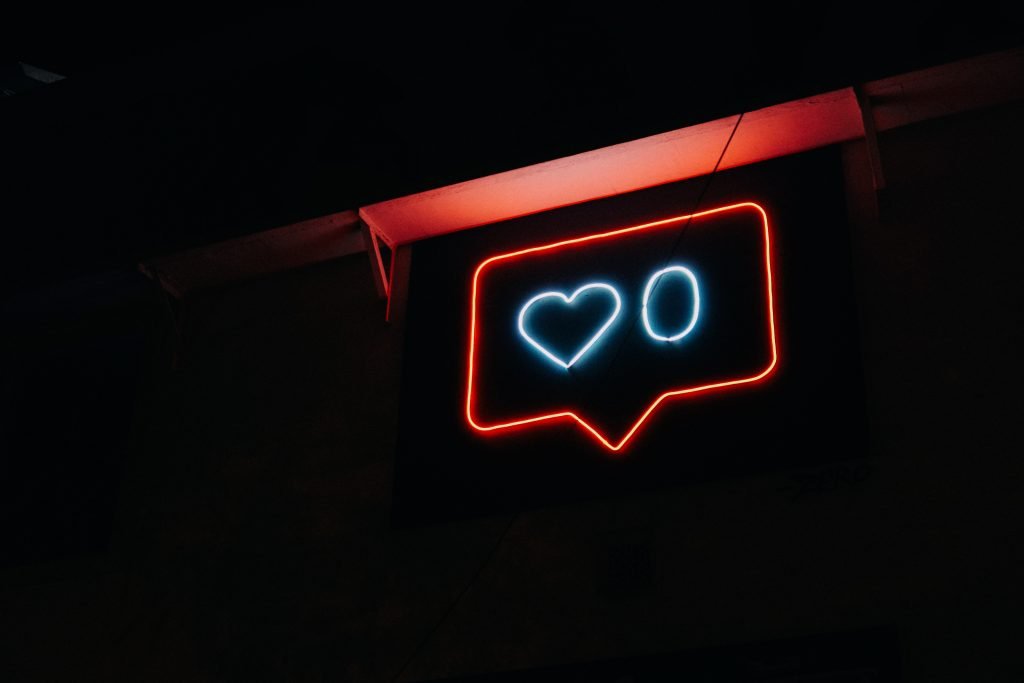 A light up neon sign of a "like" emoji from social media, lights up a dark space.